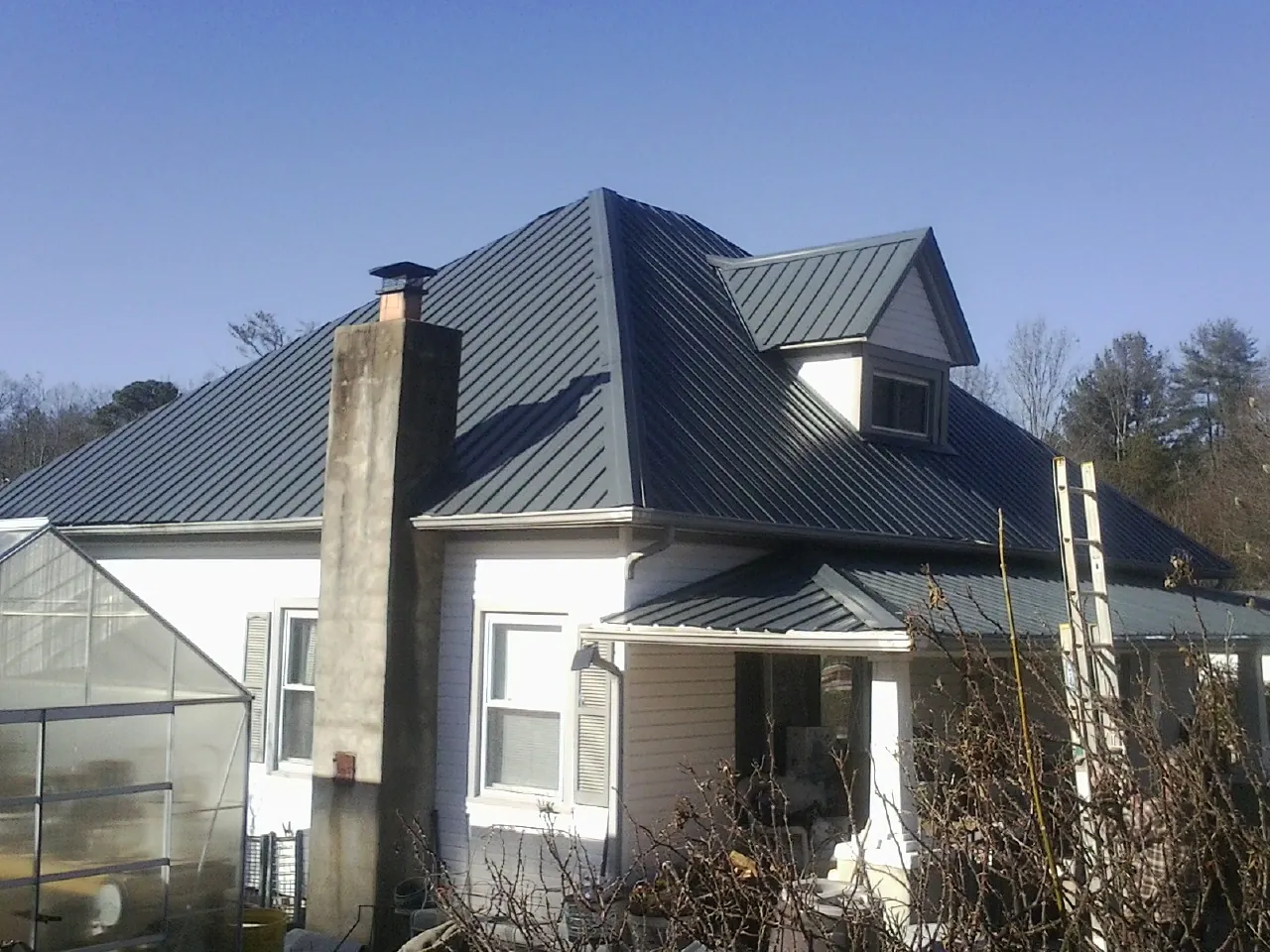 Dark blue standing seam metal roof on a white farmhouse with dormer — Slate & Tile Roof Repair by Roofing Brothers in Angleton