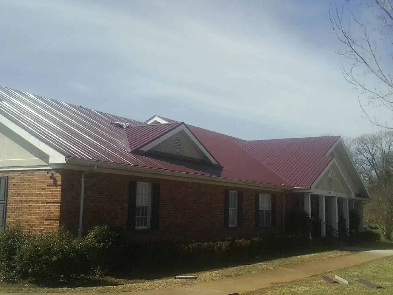 Red metal roof with gabled entries on a long brick building, from a Hail Damage Roof Repair job in Angleton