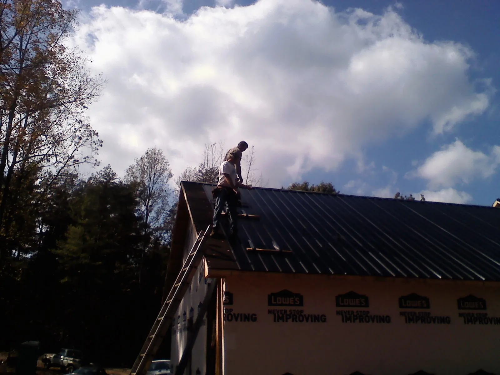 Roofer fastening dark metal panels high against a cloudy sky, from a Roof Inspection job in Angleton